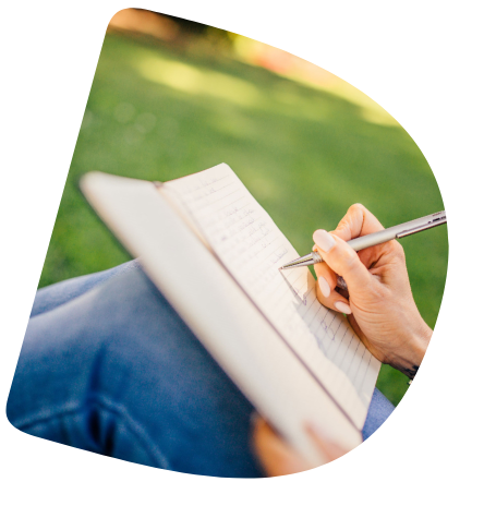 Ein Notizbuch liegt auf den Knien einer Frau. Sie schreibt in das Buch.