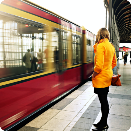 Eine Frau in einem gelben Regenmantel steht an einem Bahnhof während ein Zug einfährt.