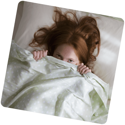 Neurodermitis betroffene Frau versteckt sich unter der Bettdecke