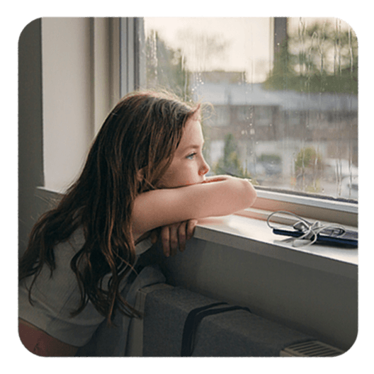 Von Neurodermitis betroffenes Mädchen blickt traurig aus dem Fenster