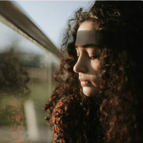 Junge Frau steht traurig am Fenster